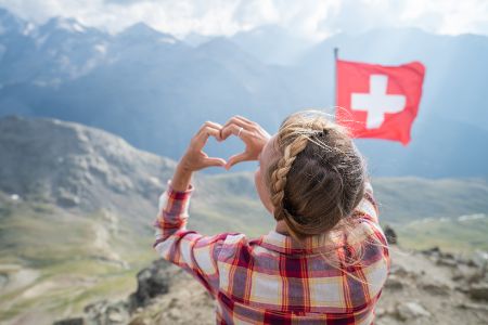 Frau formt Herz aus Händen vor Bergkulisse und Schweizer Flagge